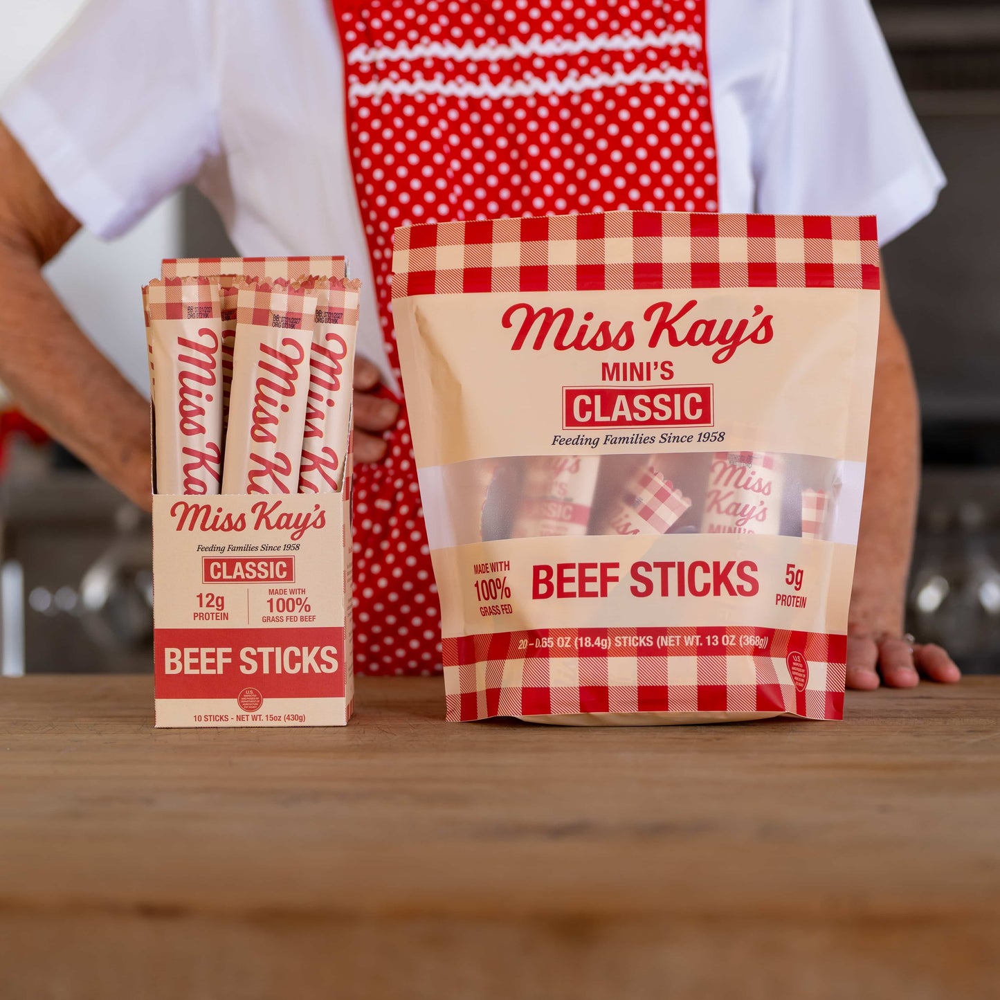 Miss Kay's Classic beef sticks box on a kitchen counter with Miss Kay in her red polka-dot apron behind