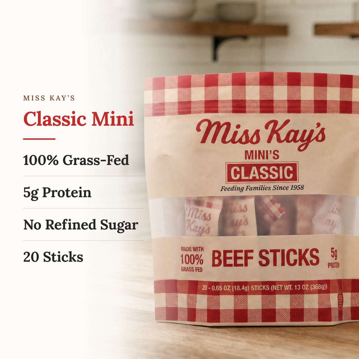 Miss Kay's Classic Mini Beef Sticks in a 13 oz bag, shown on a light wood surface with text callouts on the left detailing '100% Grass-Fed', '5g Protein', 'No Refined Sugar', and '20 Sticks'.